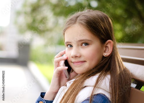 Portrait of cute smiling little girl child calling by cell phone smartphone