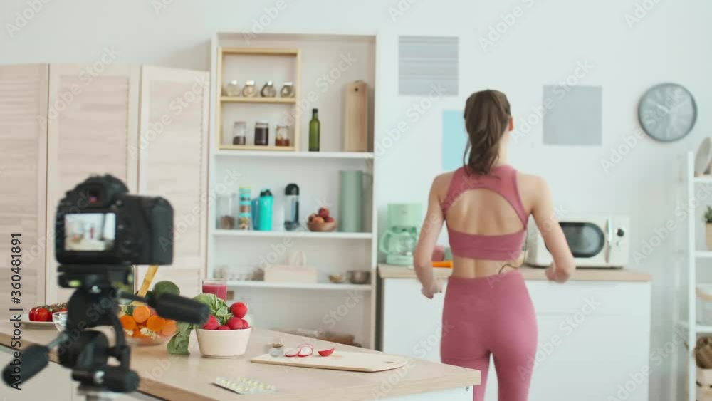 Medium shot of young Caucasian sporty woman standing at kitchen worktop, cutting radish and then taking bowl with broccoli and showing it on camera Medium shot of young Caucasian sporty woman standing at kitchen worktop, cutting radish and then taking bowl with broccoli and showing it on camera