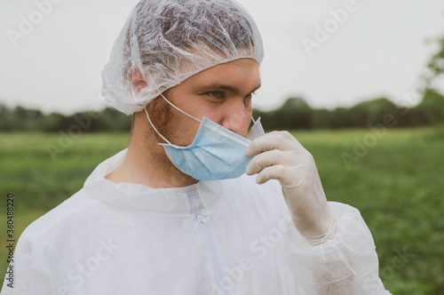 A man adjusts a mask on his face in the outdoors. Quarantine, world pandemic, COVID-19 photo