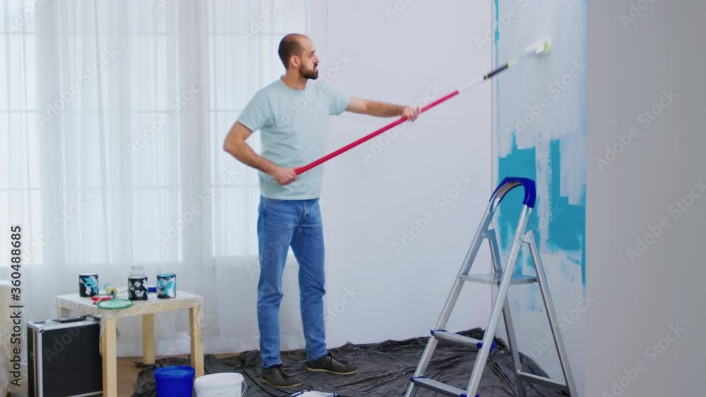 Handyman renovating house. Painting wall with roller brush dipped in white paint. Handyman renovating. Apartment redecoration and home construction while renovating and improving. Repair and Handyman renovating house. Painting wall with roller brush dipped in white paint. Handyman renovating. Apartment redecoration and home construction while renovating and improving. Repair and
