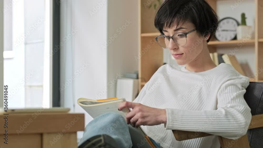 A beautiful young businesswoman wearing eyeglasses is writing something in her copybook sitting in the modern office A beautiful young businesswoman wearing eyeglasses is writing something in her copybook sitting in the modern office