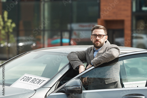 Portrait of mature bearded businessman in eyeglasses looking at camera while standing near the car outdoors