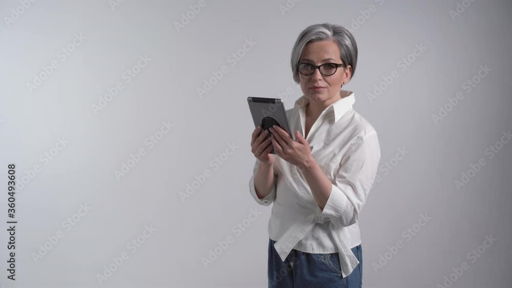 Cheerful business woman works on digital tablet on white background. Mature lady in white looking at camera. Business or Education concept. Prores 422. Cheerful business woman works on digital tablet on white background. Mature lady in white looking at camera. Business or Education concept. Prores 422.
