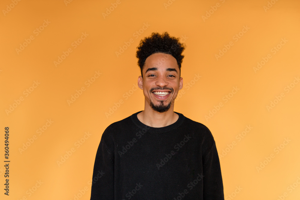 Studio portrait of afro american man wearing black pullover smiling over orange background. Portrait of dark-skinned cheerful man. Front view.