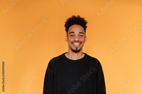 Obraz na płótnie Studio portrait of afro american man wearing black pullover smiling over orange background. Portrait of dark-skinned cheerful man. Front view. w salonie