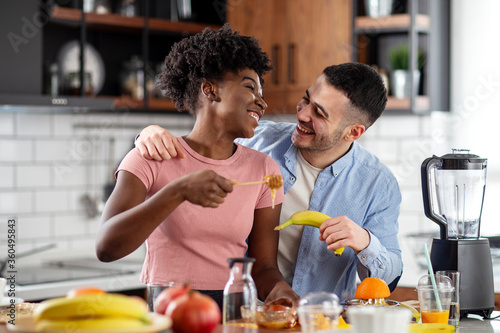 Multiethnic couple preparing healthy smoothie with tropical fruits and smile in kitchen