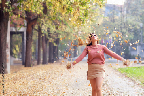 Beautiful young woman throwing leaves in public park and smile