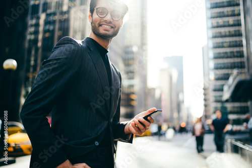 Cropped image of successful proud CEO dressed in stylish formal wear laughing at camera walking in urban setting of Manhattan.Positive entrepreneur with dital smartphone in hands strolling on street photo