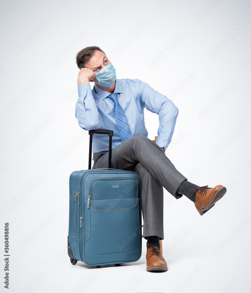 Man in a respiratory mask, shirt and tie sits with a suitcase waiting for a flight. Pandemic Travel concept. Man in a respiratory mask, shirt and tie sits with a suitcase waiting for a flight. Pandemic Travel concept.