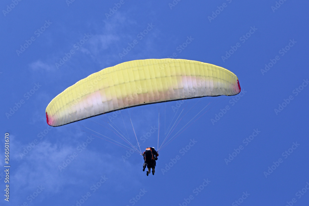 Tandem Paraglider flying wing in a blue sky Tandem Paraglider flying wing in a blue sky