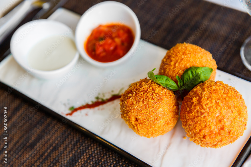 Meatballs in breadcrumbs decorated with mint leaves are served with sauces in a close-up white plate. Healthy food.
