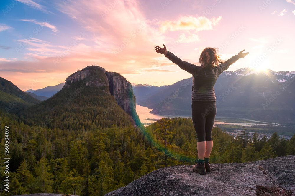 Adventurous Girl on top of a Mountain with Canadian Nature Landscape in background during a sunny sunset. Taken in Squamish, North of Vancouver, British Columbia, Canada.