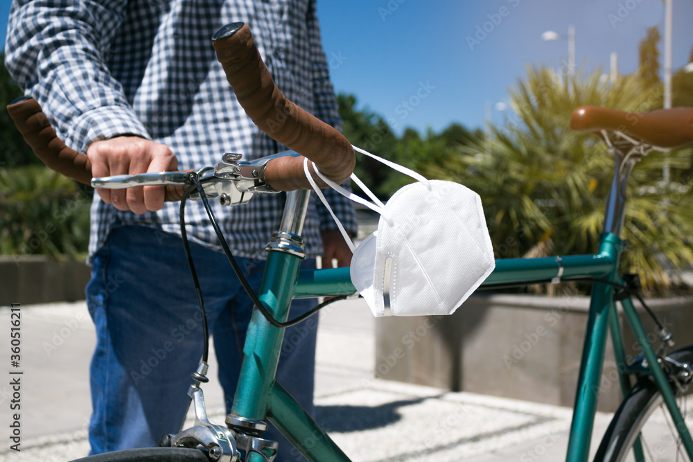 Man holding a fixed gear bicycle in the street while hanging a mask from the handlebars. Selective focus.