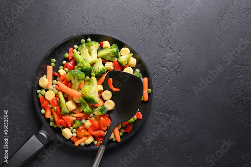 Frozen vegetables in frying pan on black background. View from above.