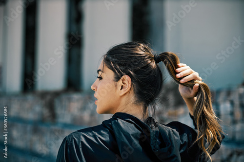 Female runner standing and adjusting ponytail. Urban exterior.