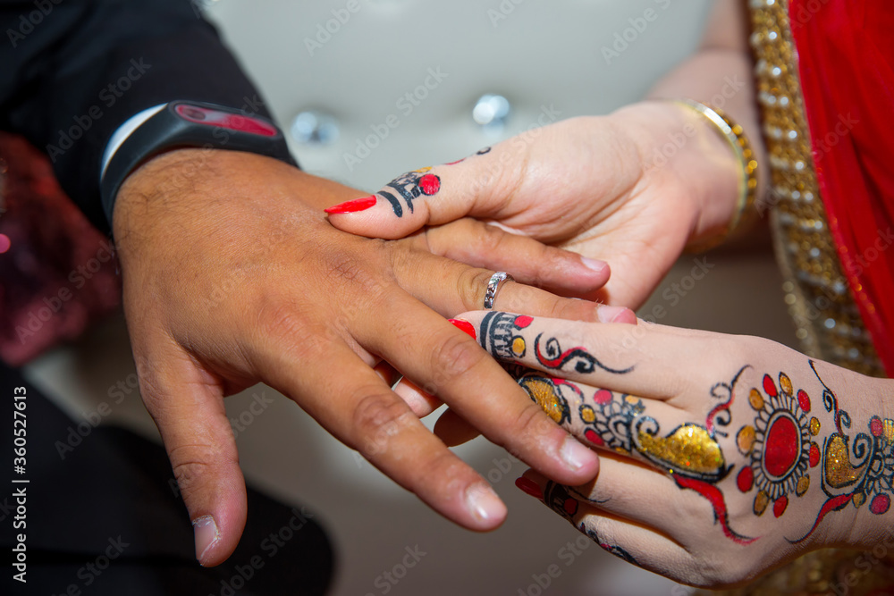 A bride is wearing a ring on the groom's finger. Indian Wedding.