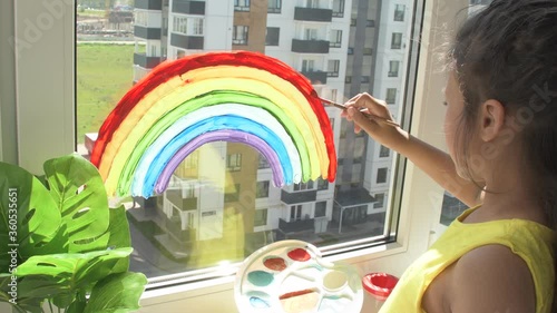 Girl painting rainbow on window during quarantine at home. photo