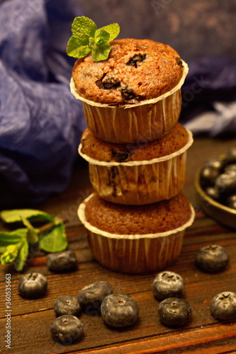 Several fragrant muffins with blueberries are on the table, next to blueberries and mint.