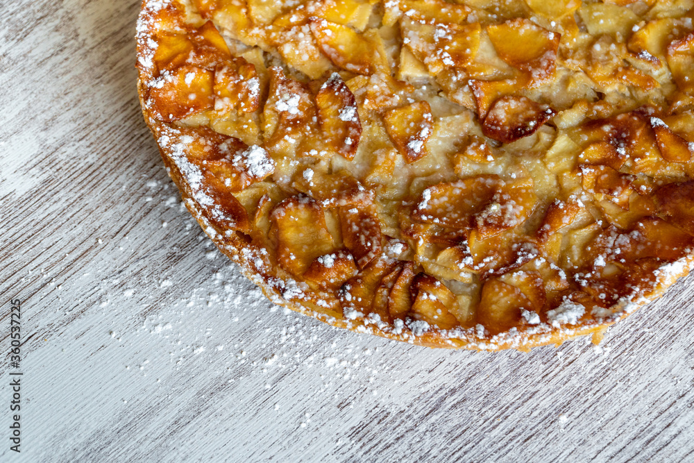 Homemade baking. Freshly baked apple pie on a light wooden background sprinkled with icing sugar.