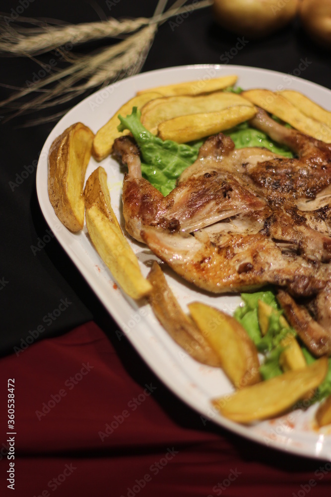Chicken tabaka with fried potatoes and greens on a color background. Chicken tabaka with fried potatoes and greens on a color background.