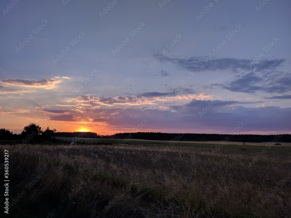 beautiful romantic orange sunset over the empty field with clouds in countryside