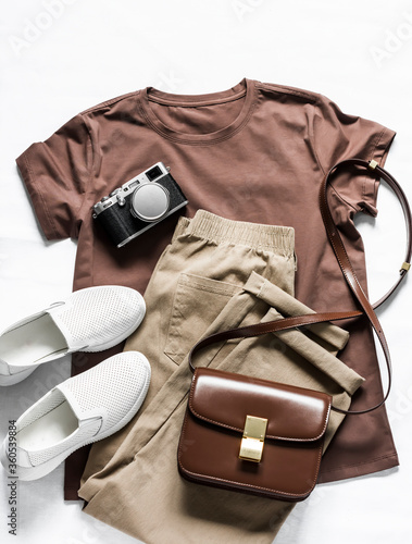 Brown t-shirt, cotton joggers jeans, white sneakers, leather cross body bag and camera on a light background, top view. Fashion beauty concept