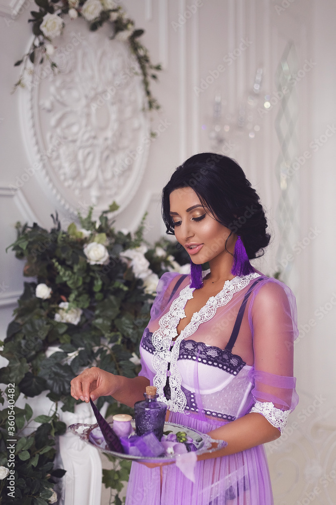 A beautiful brunette girl in a white and lilac transparent boudoir dress. Preparing for the wedding, bride's morning.