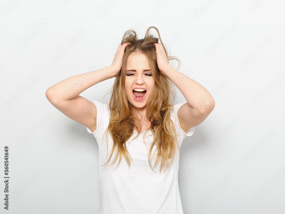 Angry young casual blond woman strong screaming with wide open mouth on blue background with empty copy space Angry young casual blond woman strong screaming with wide open mouth on blue background with empty copy space