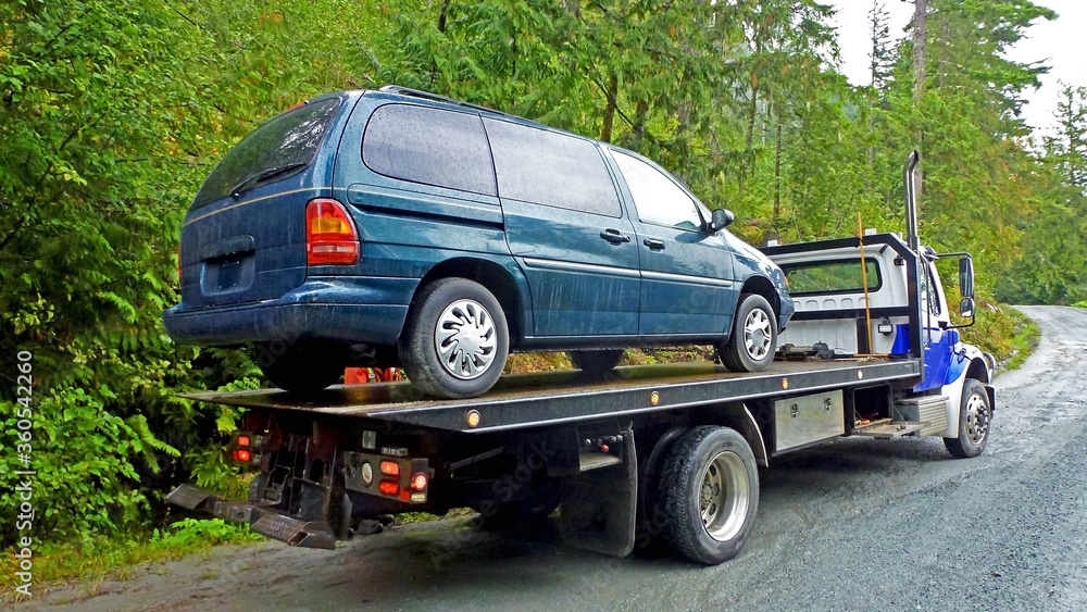 Towing service - the blue tow truck with the loaded old damaged car which stopped working in the middle of forest on the rough off road. Back view Towing service - the blue tow truck with the loaded old damaged car which stopped working in the middle of forest on the rough off road. Back view