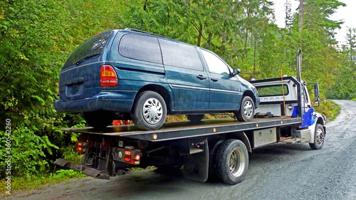 Towing service - the blue tow truck with the loaded old damaged car which stopped working in the middle of forest on the rough off road. Back view © Klara