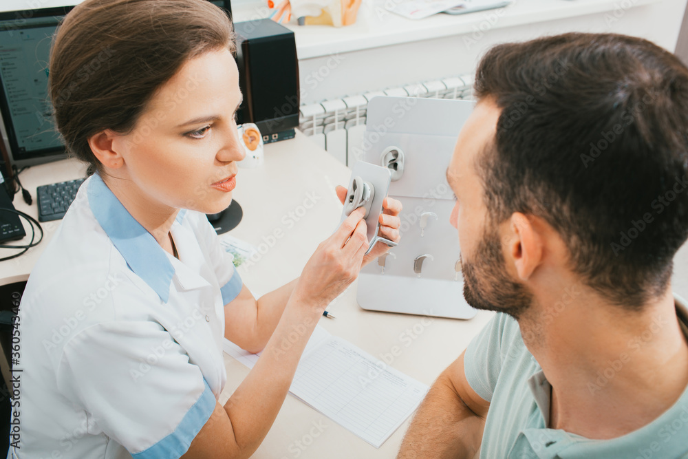 Fototapeta premium The doctor of an audiologist tells the patient about the hearing aid. Selection of hearing solutions, hearing treatment, in-ear hearing aids