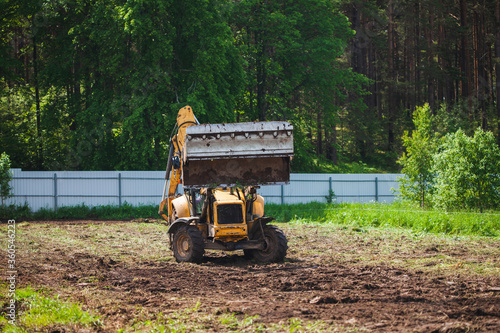 Clearing and leveling a private land plot. Yellow excavator with a large wide open bucket