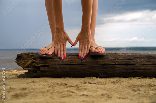 Legs and hands of a girl on a log that lies on the sand by the water