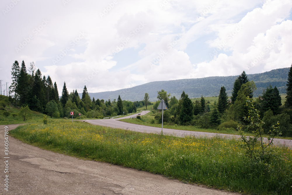 Landscape of asphalt road in the mountains with roadsign turn right. Many green trees. Vacation by car. 