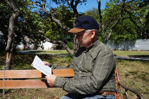 man reads a book on a park bench in summer