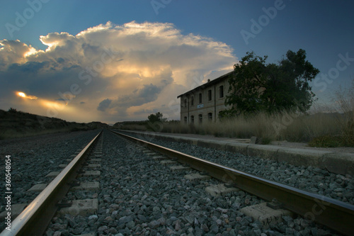 Vía del ferrocarril en estación abandonada, con tormenta al fondo.
