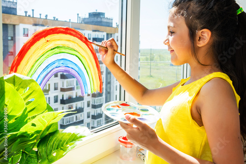 Girl painting rainbow on window during quarantine at home. photo