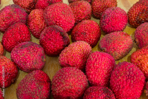 top view and close up of many red lychees on a wooden colored background