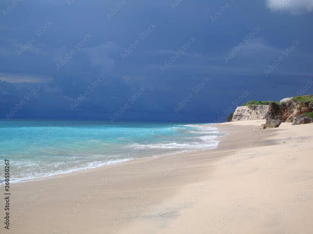 cotrast between turqiouse sea and dark dramatic stormy sky, coastline with white sand and big rocks, breathtaking view, copyspace for text. Stunning places for traveling.