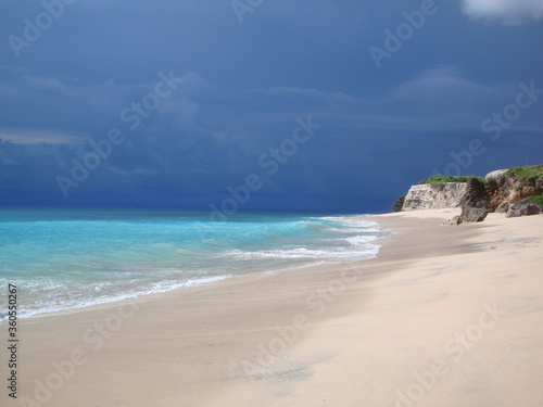 Fototapeta Naklejka Na Ścianę i Meble -  cotrast between turqiouse sea and dark dramatic stormy sky, coastline with white sand and big rocks, breathtaking view, copyspace for text. Stunning places for traveling.