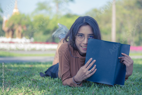 Young Asian female student woman lying on the lawn with book.