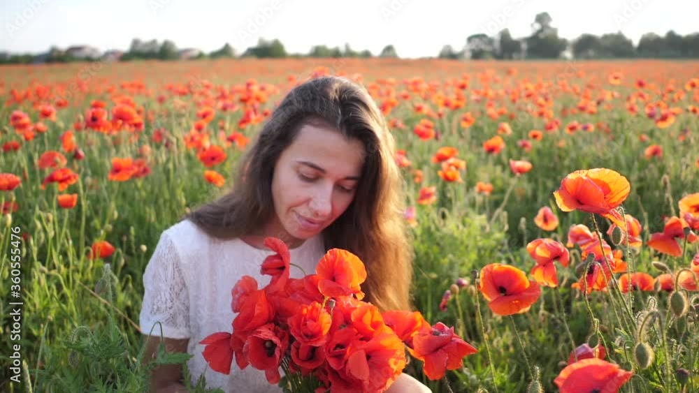 Young brunette woman in white dress stands in the middle of the field of poppies. Charming lady with incredible smile with bouquet of poppies in hands. Slow motion Full HD Young brunette woman in white dress stands in the middle of the field of poppies. Charming lady with incredible smile with bouquet of poppies in hands. Slow motion Full HD