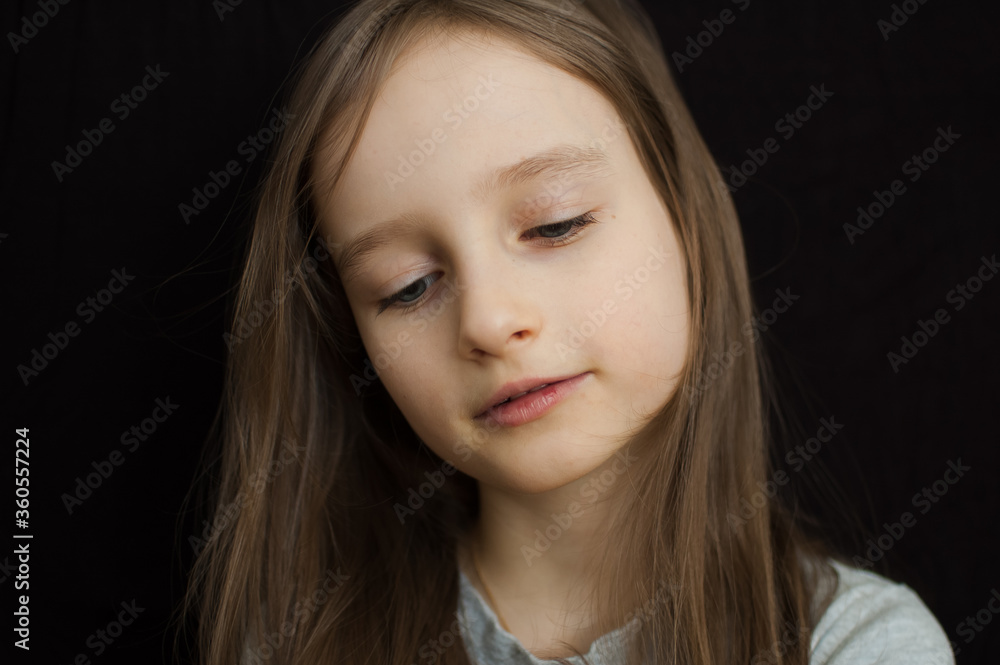 Portrait of a little sad girl with long blond hair and closed eyes on black background in studio Portrait of a little sad girl with long blond hair and closed eyes on black background in studio