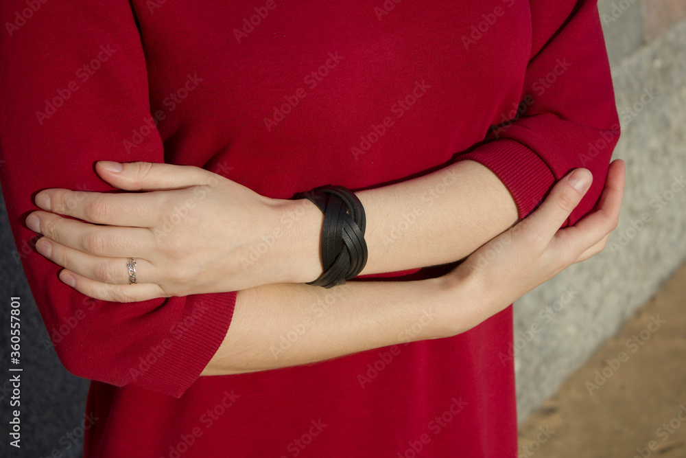 female hands with a leather bracelet  on a background of a red dress
