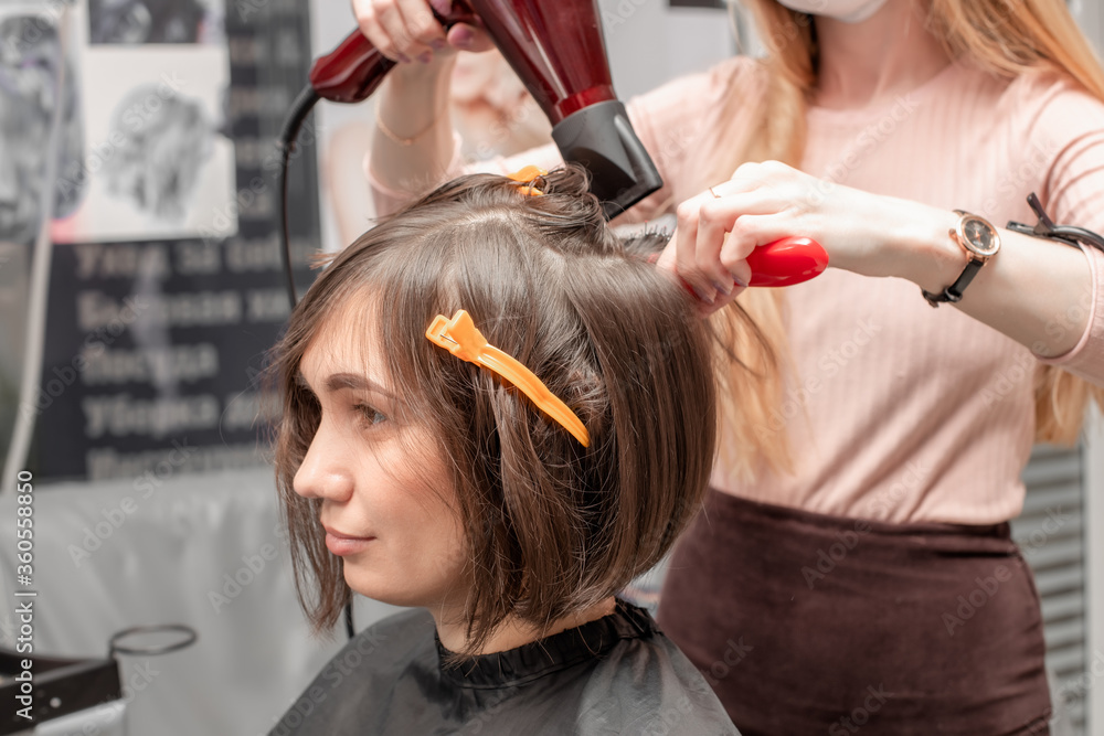 Fototapeta premium Barbershop. Hairdresser girl doing hairstyle to a young woman
