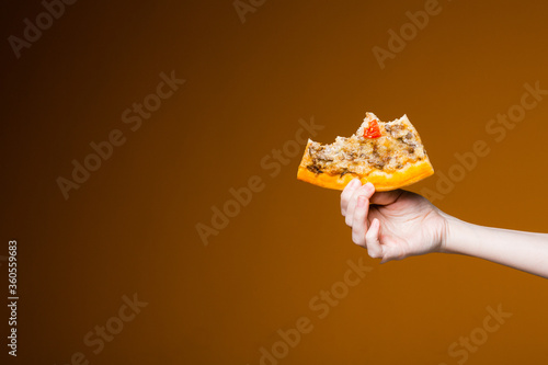 Womans hand on an orange background holding a bitten slice of pizza is like a pizzeria and fast food