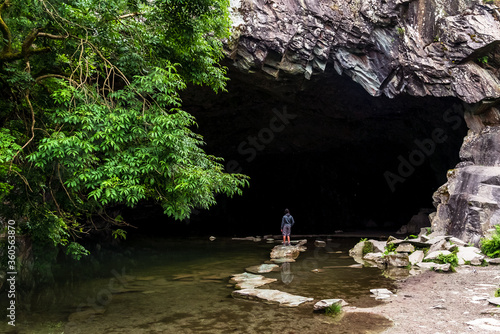 Boy standing on stepping stones at the mouth of a water filled cave which is carved out of slate. English Lake District.