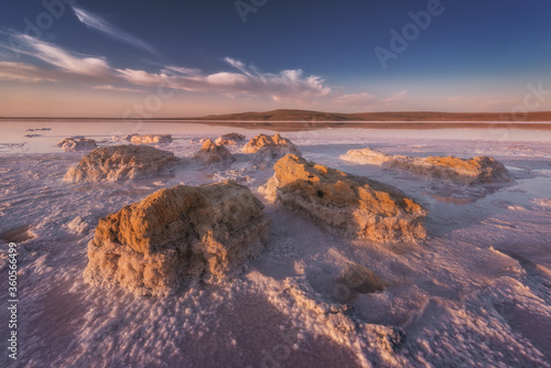 Pink salt lake at sunset with a salt-covered stones in the foreground. Fantastic natural landscape with copy space on the sky. 