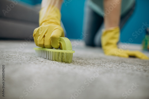 Close up of housewife in yellow rubber gloves cleaning carpet from spots with brush. Concept of working process and household.