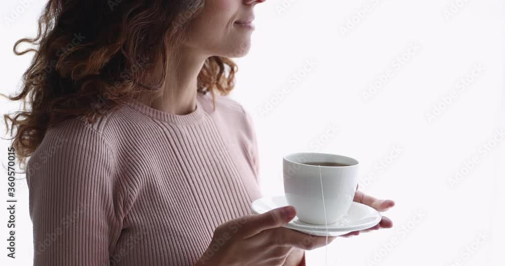 Close up young happy woman holding cup of hot black bag tea in hands, standing near window. Smiling peaceful lady spending morning time with drink, planning workday or enjoying weekend time alone. Close up young happy woman holding cup of hot black bag tea in hands, standing near window. Smiling peaceful lady spending morning time with drink, planning workday or enjoying weekend time alone.